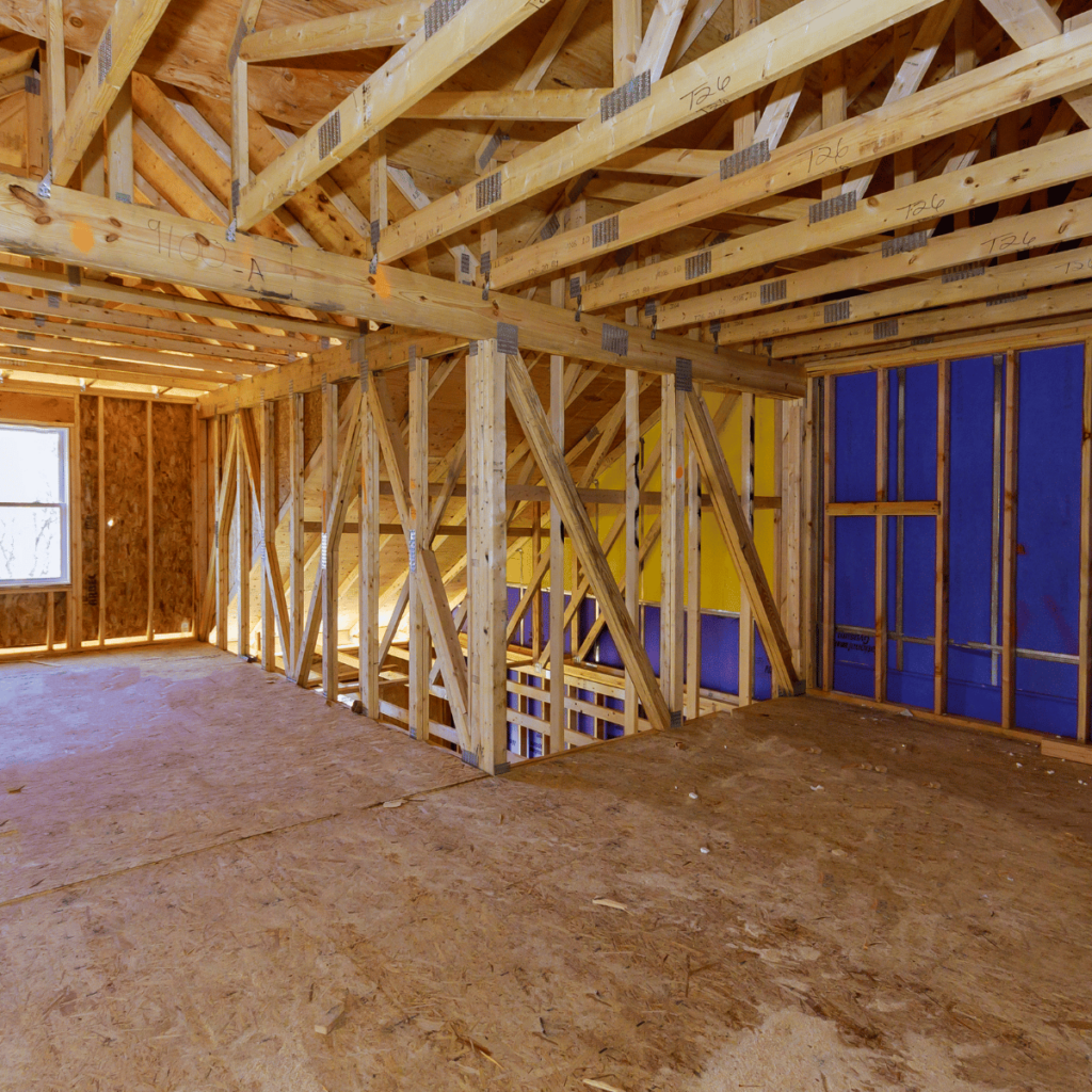 Interior framing of a home addition under construction with exposed wooden beams and plywood flooring.