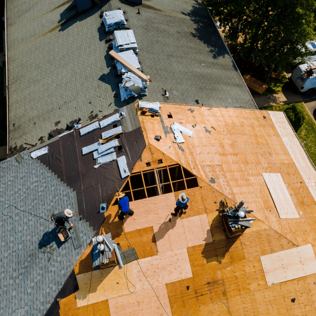 Workers installing roof sheathing and shingles on a second story addition.