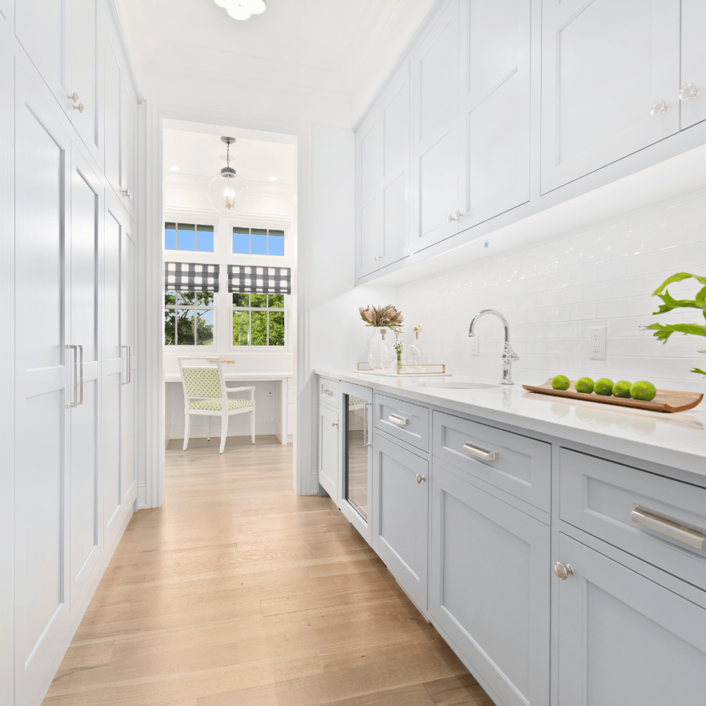 Narrow kitchen with white cabinets, wood floors, and striped window shades.