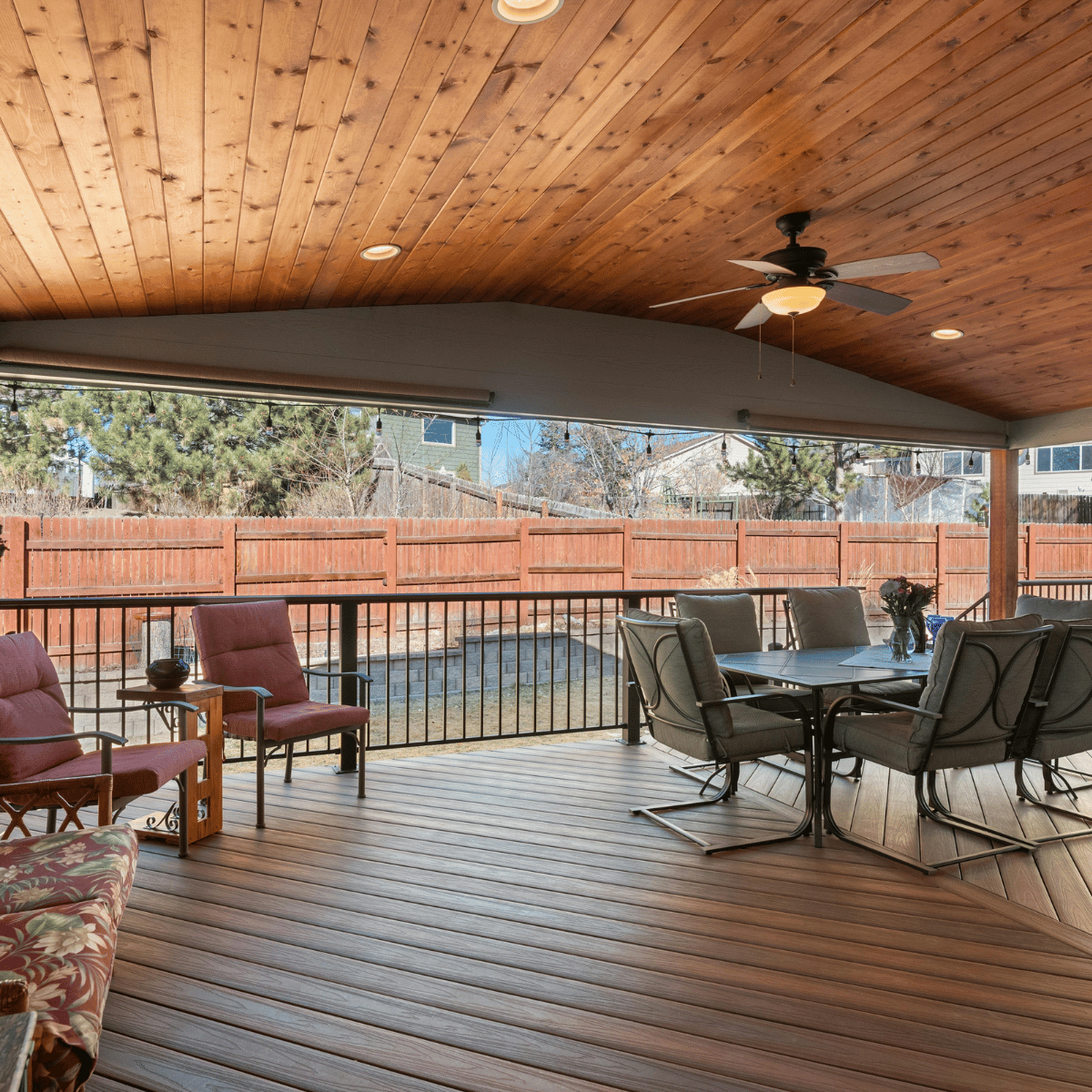 Cozy covered porch with a wooden ceiling, ceiling fan, and outdoor dining and lounge seating overlooking a fenced backyard.