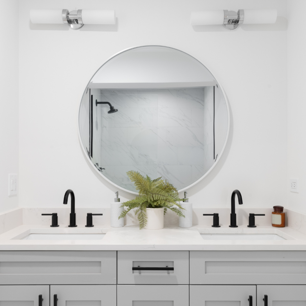 Double bathroom vanity with round mirror and black faucets.