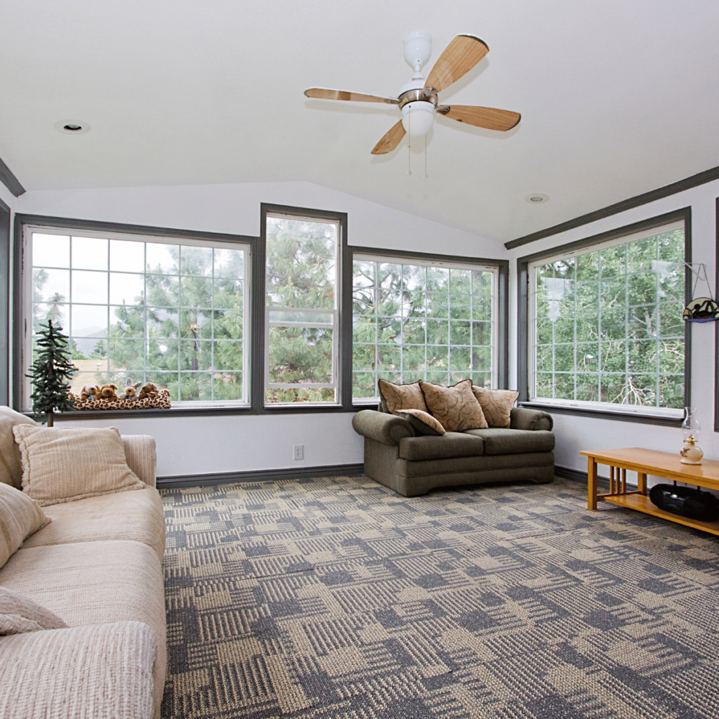 Family sunroom with carpet flooring, ceiling fan, and large windows.