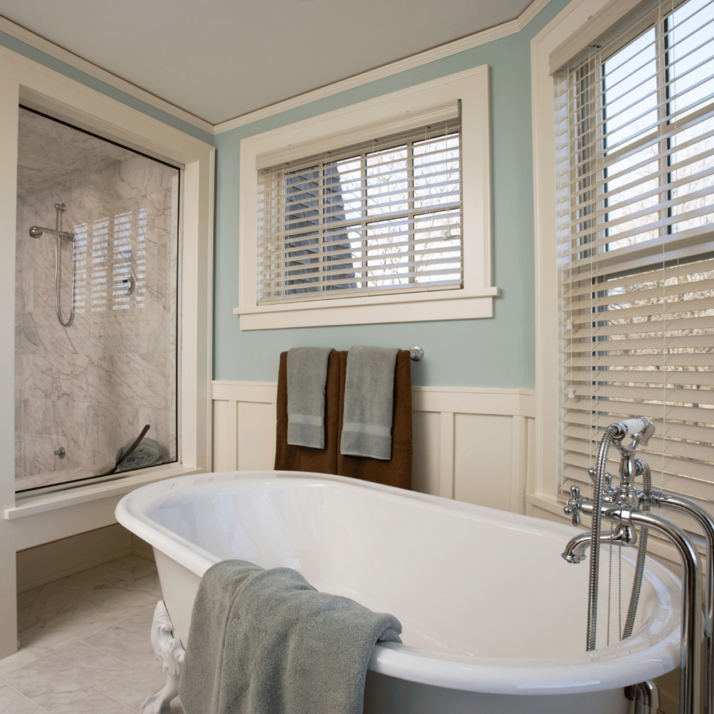 Freestanding bathtub with claw feet next to a glass shower in a bright bathroom.