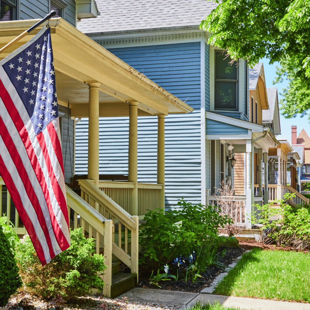 Row of historic homes with American flag on porch and lush green landscaping.