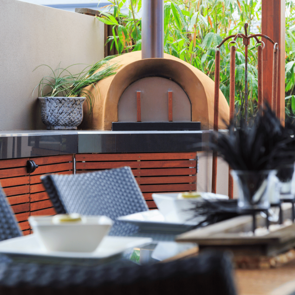 A dome-shaped wood-fired outdoor pizza oven with a chimney, surrounded by sleek black countertops and wood cabinetry.
