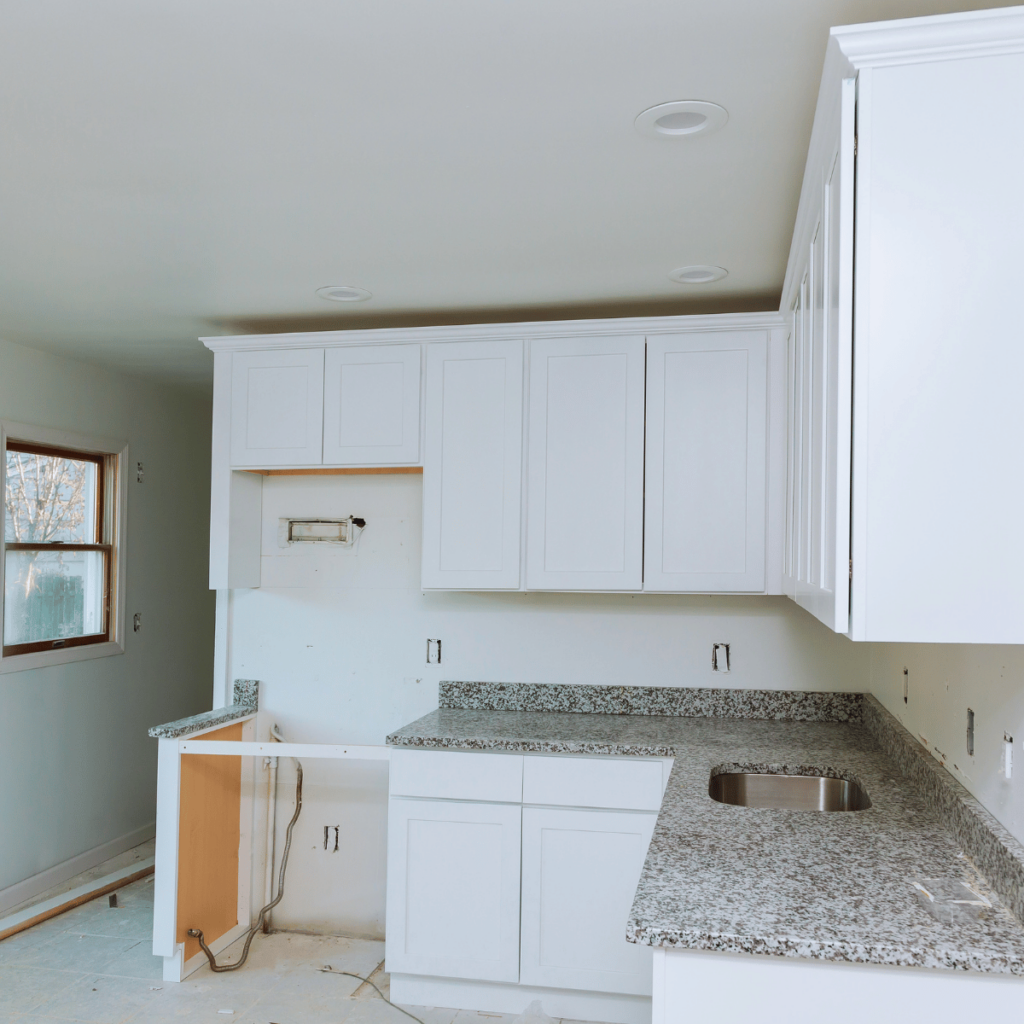 Prefabricated white kitchen cabinets with granite countertops during installation.