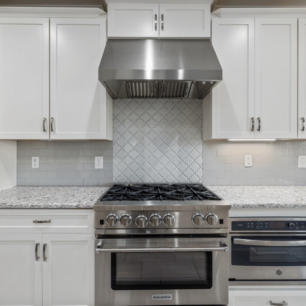 Semi-custom white kitchen cabinets with patterned tile backsplash and stainless stove.