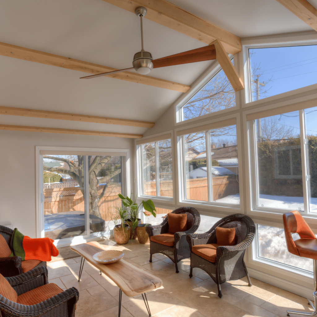Vaulted sunroom with exposed beams, wicker chairs, and large windows.