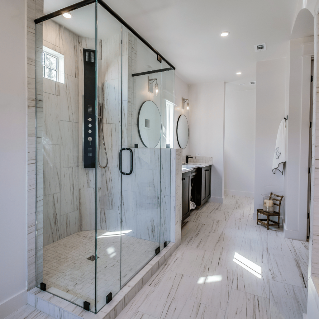 Modern bathroom with large glass walk-in shower and double vanity with round mirrors.