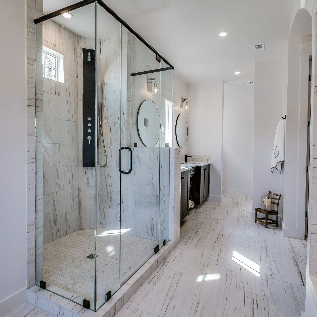 Modern bathroom with large glass walk-in shower and double vanity with round mirrors.